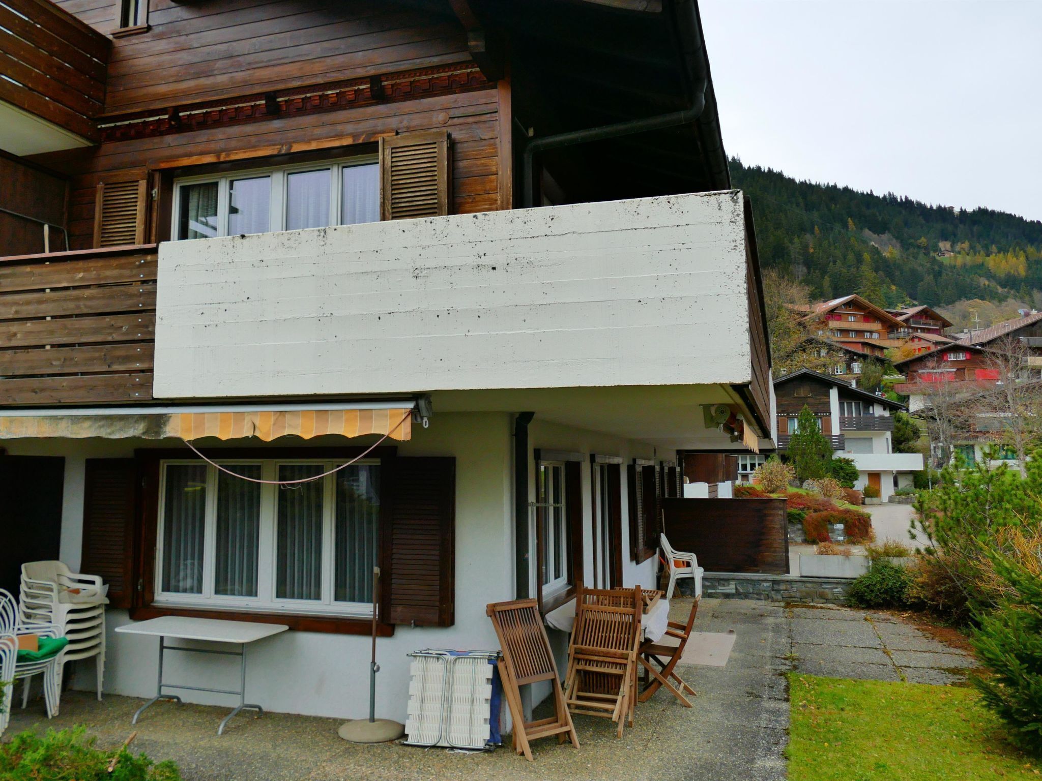 Une maison en bois à deux étages, dotée d’un balcon, d’un espace extérieur couvert aménagé en salon et offrant une vue sur un paysage montagneux.