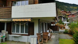 A two-story wooden house with a balcony, a covered outdoor seating area, and a view of a mountainous landscape. - Silberdistel  B09 Appartement/Fewo, Bad, WC, 3 Schlafräume 3.5 Zimmerwohnung by Interhome (Adelboden)