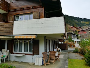 Uma casa de madeira de dois andares com varanda, área de estar coberta ao ar livre e vista para uma paisagem montanhosa.