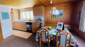 Cocina compacta con armarios de madera, una mesa de comedor con sillas, una lámpara colgante y un cuadro en la pared.