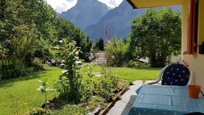Un patio con mesa y sillas, con vista a un jardín lleno de plantas y una montaña.