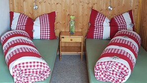 Una habitación con dos camas, cada una con una manta a cuadros, una mesita de noche de madera y un cuadro en la pared.