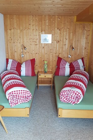 Ein Zimmer mit zwei Betten, jedes mit einer karierten Decke, einem kleinen Nachttisch und einem Bild an der Wand.