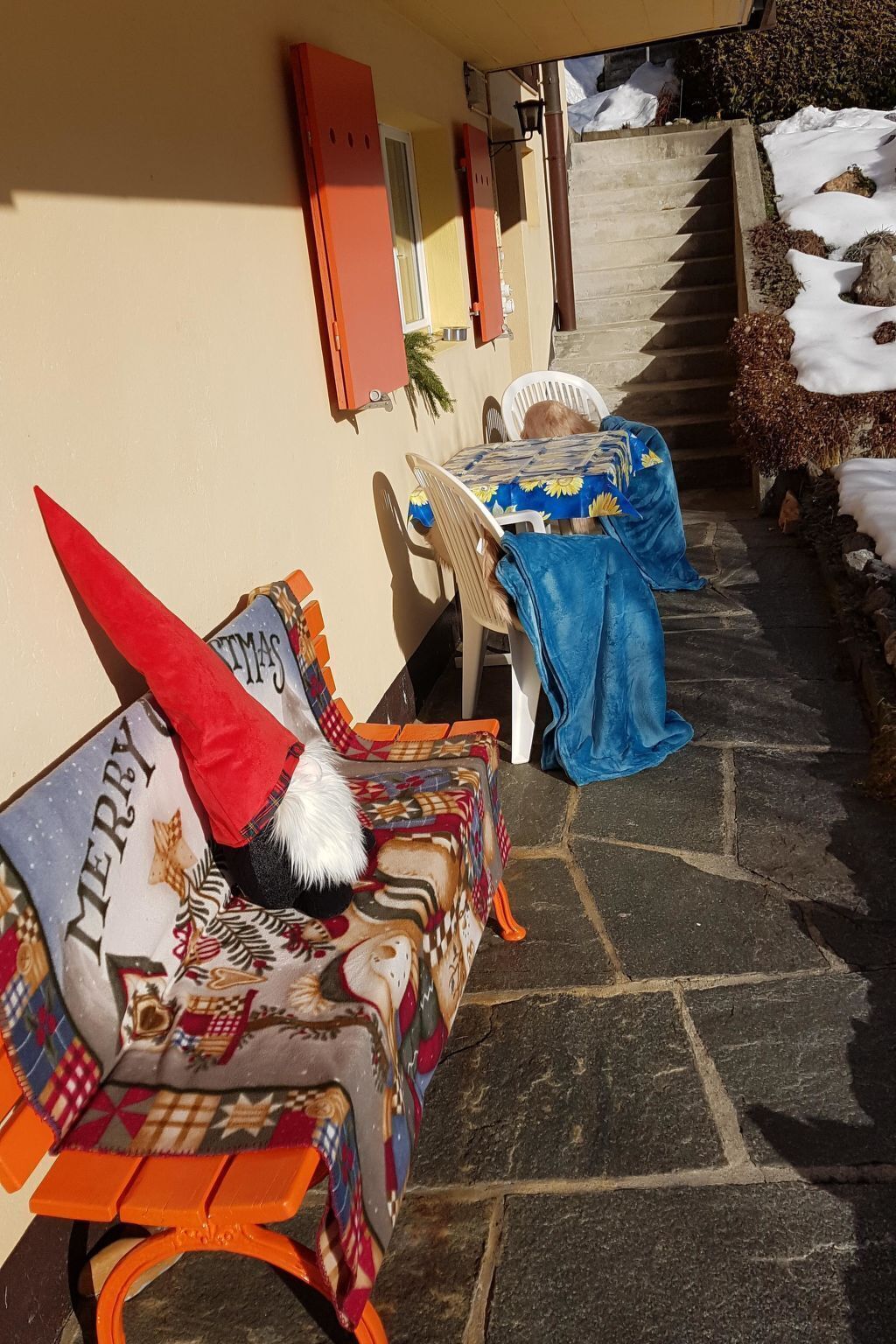 Un espace extérieur abrité, aménagé avec un banc et une table, tous deux recouverts de nappes colorées.