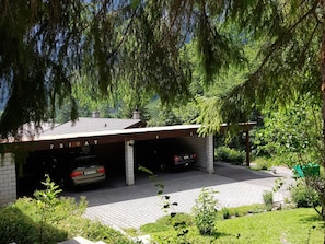 Un garage pour deux voitures, avec une façade en briques et un toit en tuiles, entouré de verdure et d’arbres.