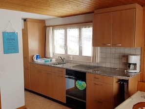 A kitchen with wooden cabinets, a sink, and a window with curtains. - Chalet Rosmarie Appartement/Fewo, Dusche, WC, 1 Schlafraum by Interhome (Kandersteg)