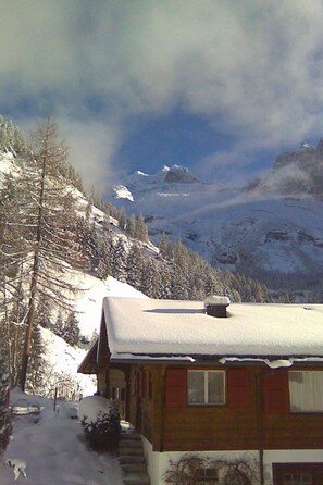Eine Holzhütte mit verschneitem Dach, umgeben von schneebedeckten Bäumen und Bergen.