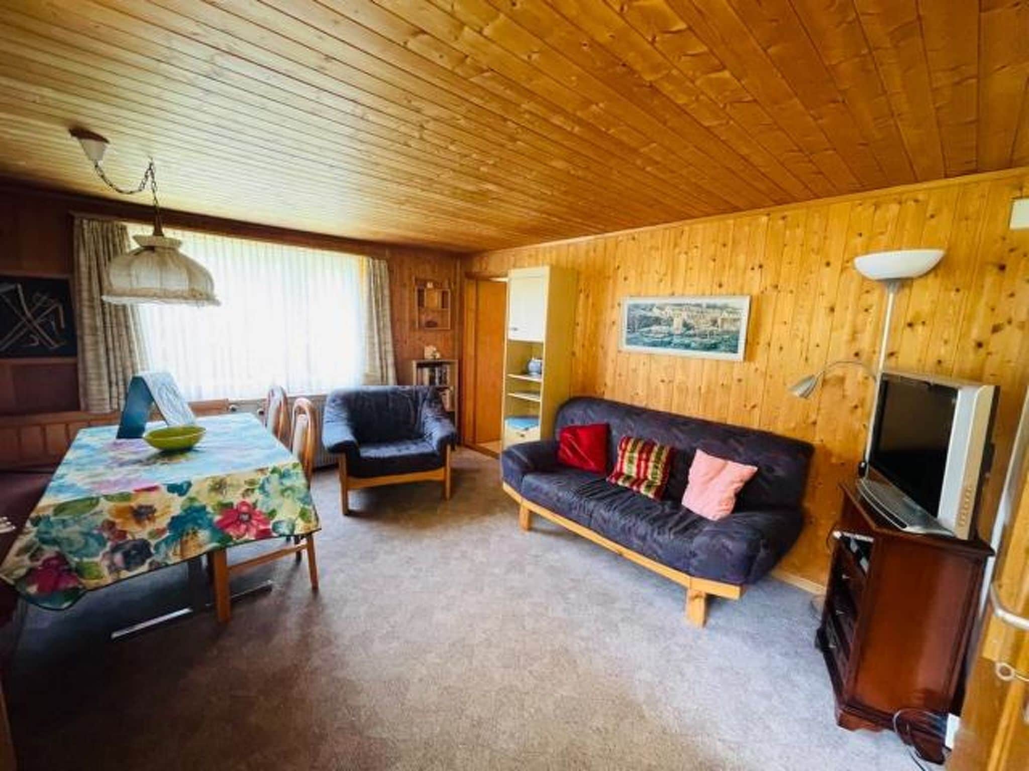 Une pièce chaleureuse avec un plafond en bois, un canapé, une table à manger avec des chaises et un téléviseur.