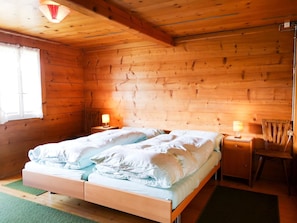 Ein Zimmer in einer Holzhütte mit einem Bett, zwei Nachttischlampen, einem Sessel und einem Fenster.
