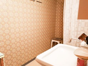 Ein Badezimmer mit gemustertem Tapeten und einem weißen Waschbecken, sowie einem kleinen Hocker.
