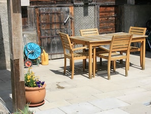 Eine Terrasse im Freien mit einem Holztisch und -stühlen, einem Blumentopf und einem blauen Gartenschlauch.