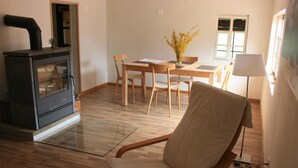 Ein Wohnzimmer mit Holzboden, einer Couch, einem Esstisch mit Stühlen, einer Küchenzeile mit Herd und einem Fenster mit Ausblick.