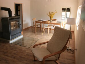 Ein Wohnzimmer mit Holzboden, einer Couch, einem Esstisch mit Stühlen, einer Küchenzeile mit Herd und einem Fenster mit Ausblick.