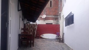 Un callejón estrecho con una puerta roja, una tabla de surf apoyada contra la pared y una antena parabólica en el techo.