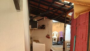 Un pasillo estrecho con piso rojo, un refrigerador blanco y una silla de plástico.