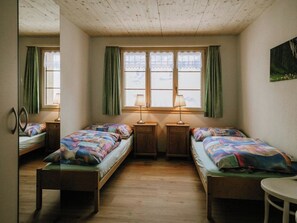 Ein Zimmer mit zwei Holzbett, einem kleinen Tisch und zwei Lampen.