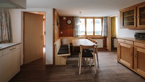 Cocina compacta con armarios de madera, una mesa de comedor con sillas, un banco empotrado y una ventana con cortinas.