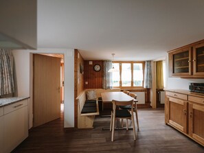 A compact kitchen with wooden cabinets, a dining table with chairs, a built-in bench, and a window with curtains. - Chalet Christeli Appartement/Fewo, Dusche oder Bad, WC, 4 oder mehr Schlafräume by Interhome (Adelboden)