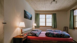 Un dormitorio con techo de madera, una cama con ropa de cama colorida, dos lámparas de noche y un ventanal con cortinas.