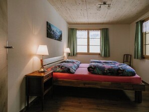 A bedroom with a wooden ceiling, a bed with colorful bedding, two bedside lamps, and a window with curtains. - Chalet Christeli Appartement/Fewo, Dusche oder Bad, WC, 4 oder mehr Schlafräume by Interhome (Adelboden)