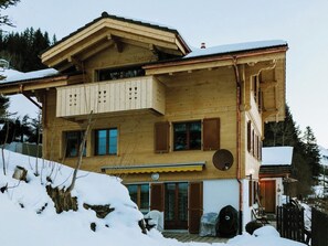 Een houten chalet met twee verdiepingen, een balkon, grote ramen en een schotelantenne.