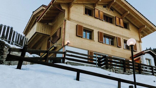 Un edificio de varios pisos con techo inclinado, contraventanas de madera y un balcón.