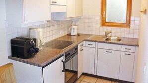 Une cuisine de taille réduite avec des meubles blancs, un four encastré, un évier et une fenêtre située au-dessus de l’évier.