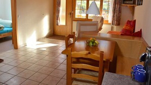 Une pièce chaleureuse avec une table à manger en bois, des chaises, un canapé, un téléviseur et une fenêtre avec des rideaux.