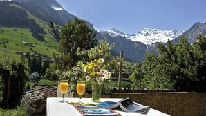 Une table avec vue sur des montagnes enneigées, un bouquet de fleurs et deux verres de jus d’orange.