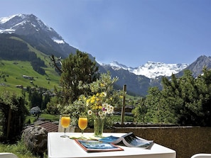 Ein Tisch mit Blick auf schneebedeckte Berge, ein Blumenstrauß und zwei Gläser Orangensaft.