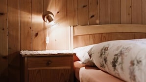 Una cama de madera con una mesita de noche, una lámpara y un cojín estampado con motivos florales.