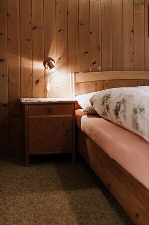 Een houten bed met een nachtkastje, een lamp en een kussen met bloemenprint.