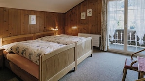 Una habitación con dos camas de madera, un radiador, una silla y una ventana con cortinas.