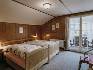 A room with two wooden beds, a radiator, a chair, and a window with curtains.