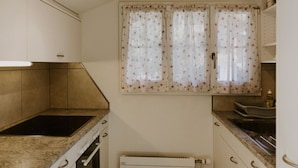 Una cocina compacta con estufa, horno integrados y una ventana con cortinas florales.
