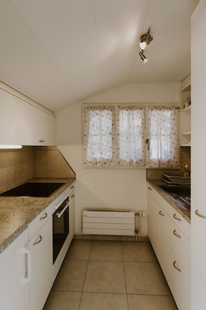 A compact kitchen with a built-in stove, oven, and a window with floral curtains.
