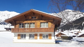 Eine zweistöckige Holzchalet mit Balkon, vor einer verschneiten Berglandschaft.