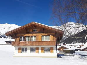 A two-story wooden chalet with a balcony, set against a snowy mountain backdrop. - Baselbiet Appartement/Fewo, Bad, WC, 3 Schlafräume 4 Zimmerwohnung by Interhome (Adelboden)