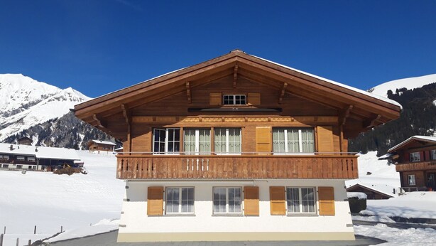 Eine Holzhütte mit Balkon vor einer verschneiten Bergkulisse.