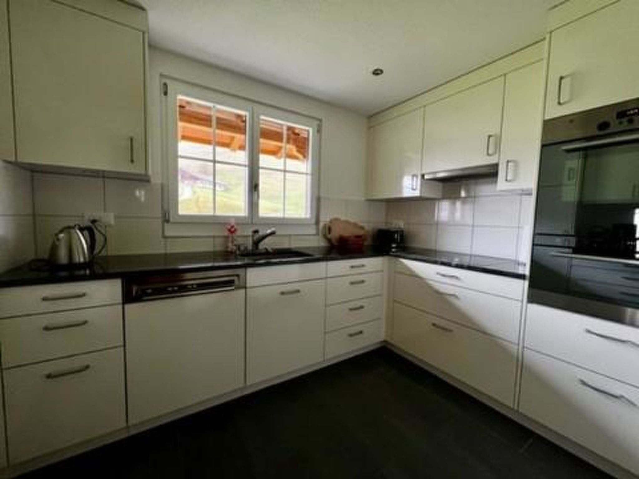 Cocina con armarios blancos, encimera negra y ventana con persianas.