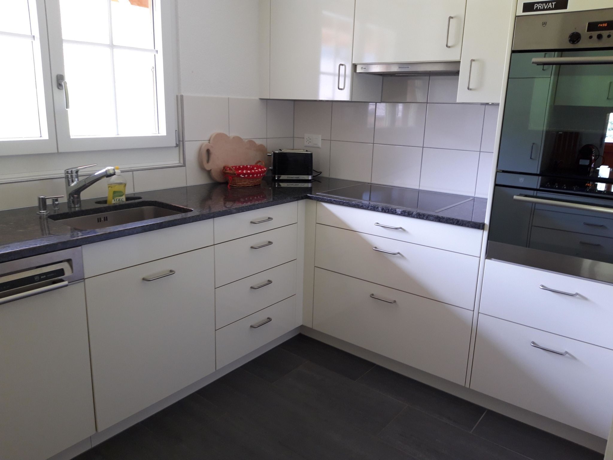 A modern kitchen with white cabinets, a stainless steel sink, a toaster, and a built-in oven.