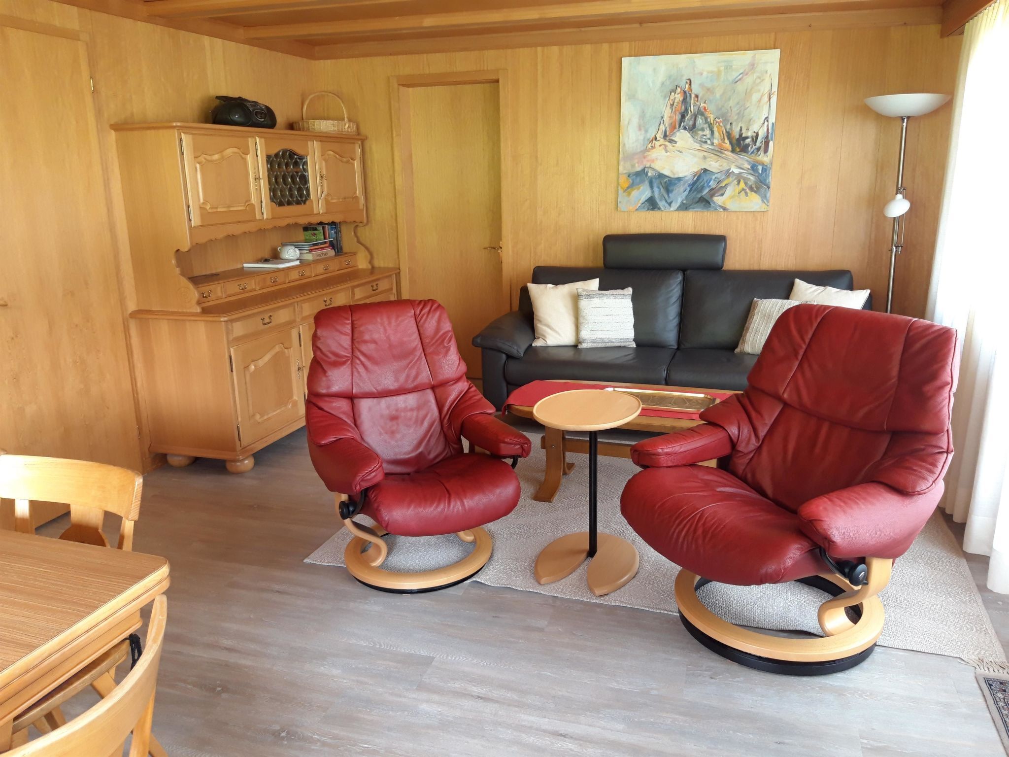 Ein Zimmer mit zwei roten Ledersesseln, einem Holzesstisch, einer Couch und einem Gemälde an der Wand.