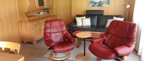 Ein Zimmer mit zwei roten Ledersesseln, einem Holzesstisch, einer Couch und einem Gemälde an der Wand.