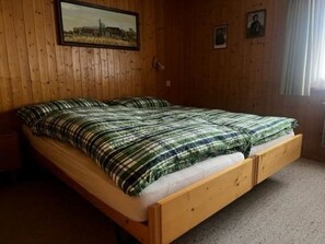 A wooden bed with a plaid bedspread in a room with wooden walls and a framed picture above the bed. - Baselbiet Appartement/Fewo, Bad, WC, 3 Schlafräume 4 Zimmerwohnung by Interhome (Adelboden)