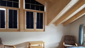 Une pièce comprenant un lit, deux chaises, une petite table et de grandes fenêtres équipées de stores.