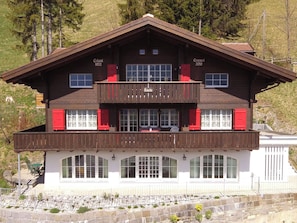 Un chalet à deux étages doté d’un balcon, de grandes fenêtres et de fondations en pierre.