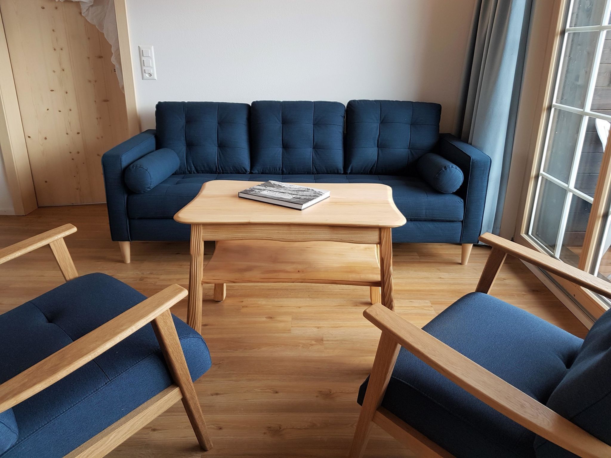 A living room with a dark blue sofa, a wooden coffee table, and matching blue upholstered chairs.
