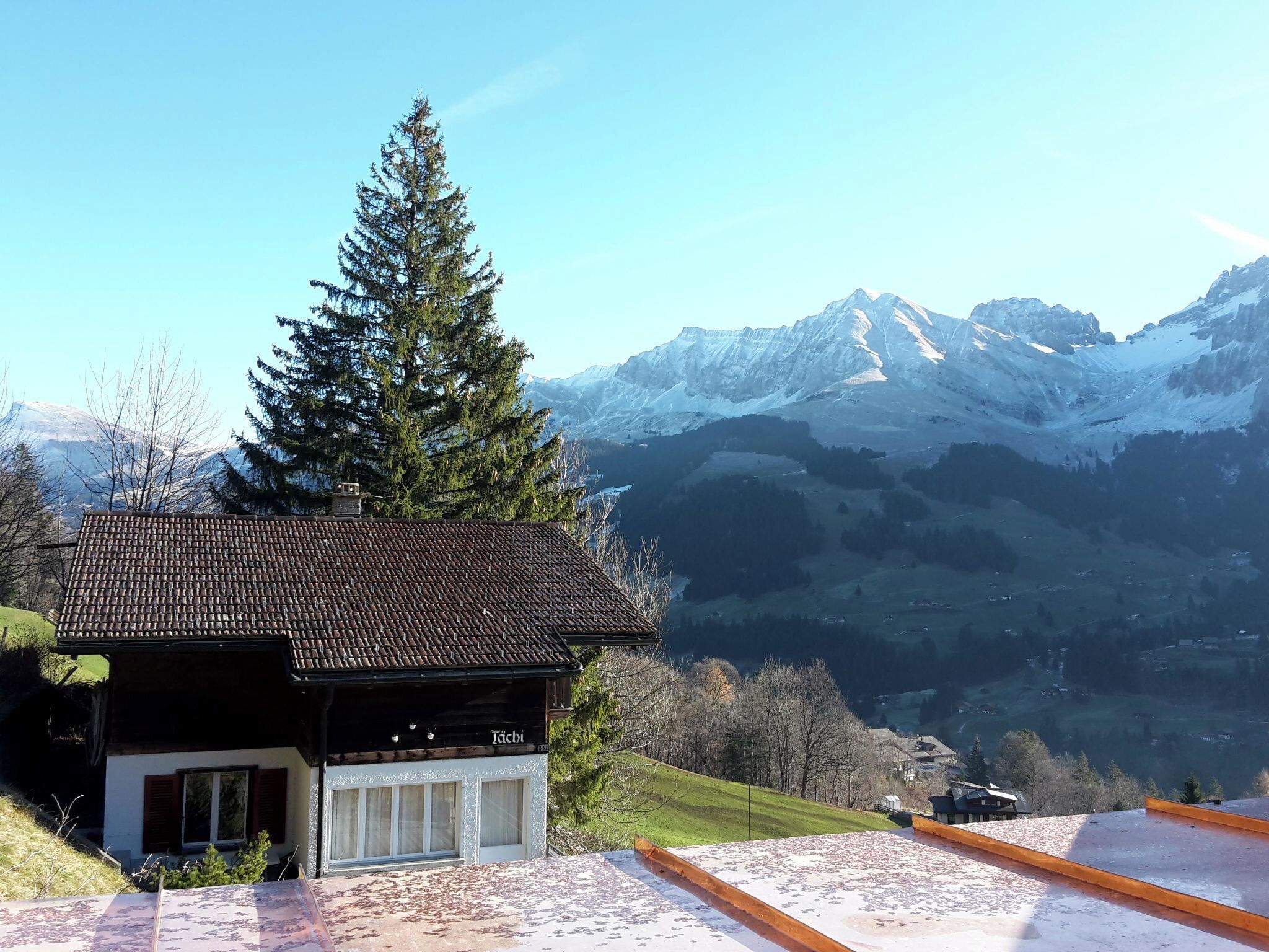 Un chalet doté d’un toit en tuiles, d’une grande fenêtre et offrant une vue sur des montagnes enneigées.