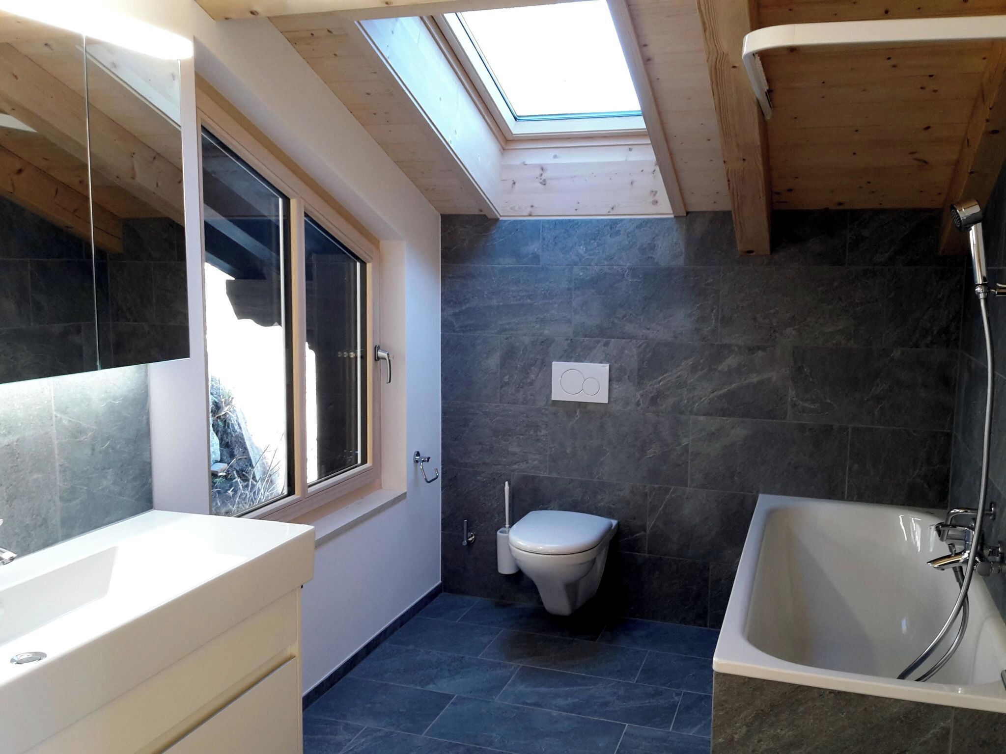 A bathroom with a skylight, a bathtub, a toilet, and a window.