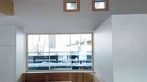 Une pièce avec un plafond en bois, une grande fenêtre donnant sur un paysage enneigé, une table en bois avec des bancs et une chaise en bois.